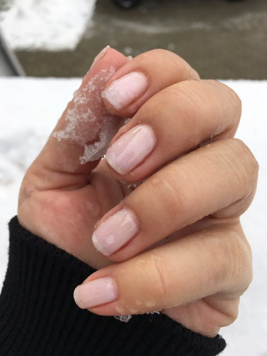 Hand mit frisch lackierten, perlmuttrosa Nägeln, im Schnee fotografiert